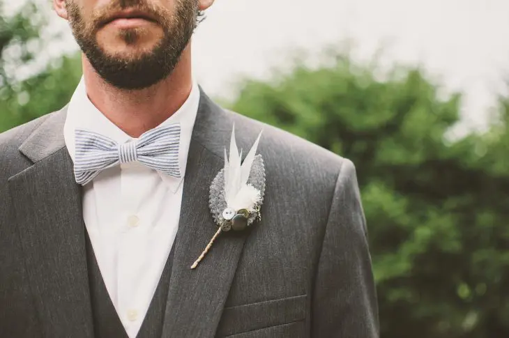 homme portant un nœud papillon bleu rayé avec costume gris et boutonnière blanche