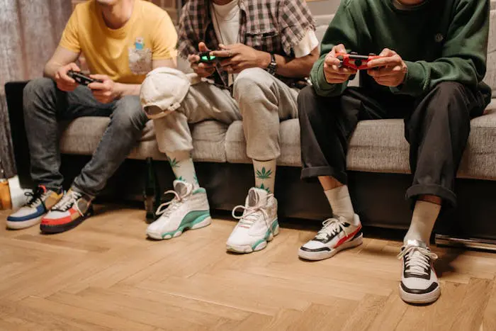 quatre hommes assis sur un canapé portant des sneakers colorées et jouant aux jeux vidéo