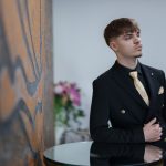 Man in a black suit with a gold tie poses.