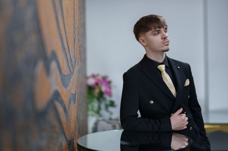 Man in a black suit with a gold tie poses.