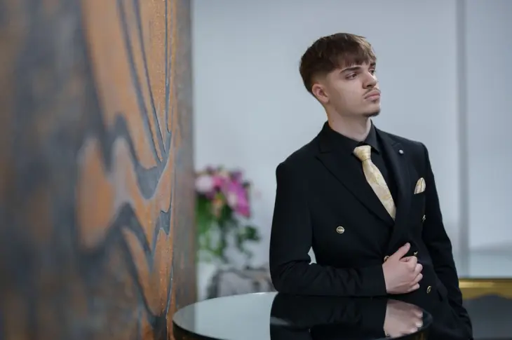 Man in a black suit with a gold tie poses.