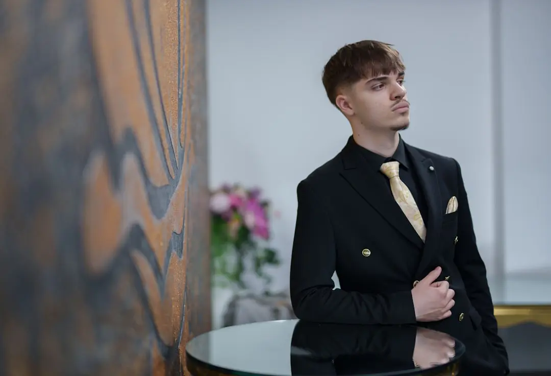Man in a black suit with a gold tie poses.